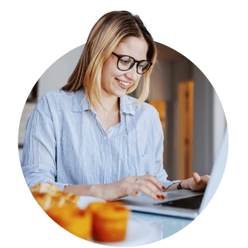 A woman with glasses smiling and typing in laptop